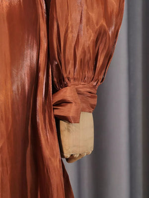 Brown ruched bodice maxi dress with draped detail and cinched cuff sleeves.