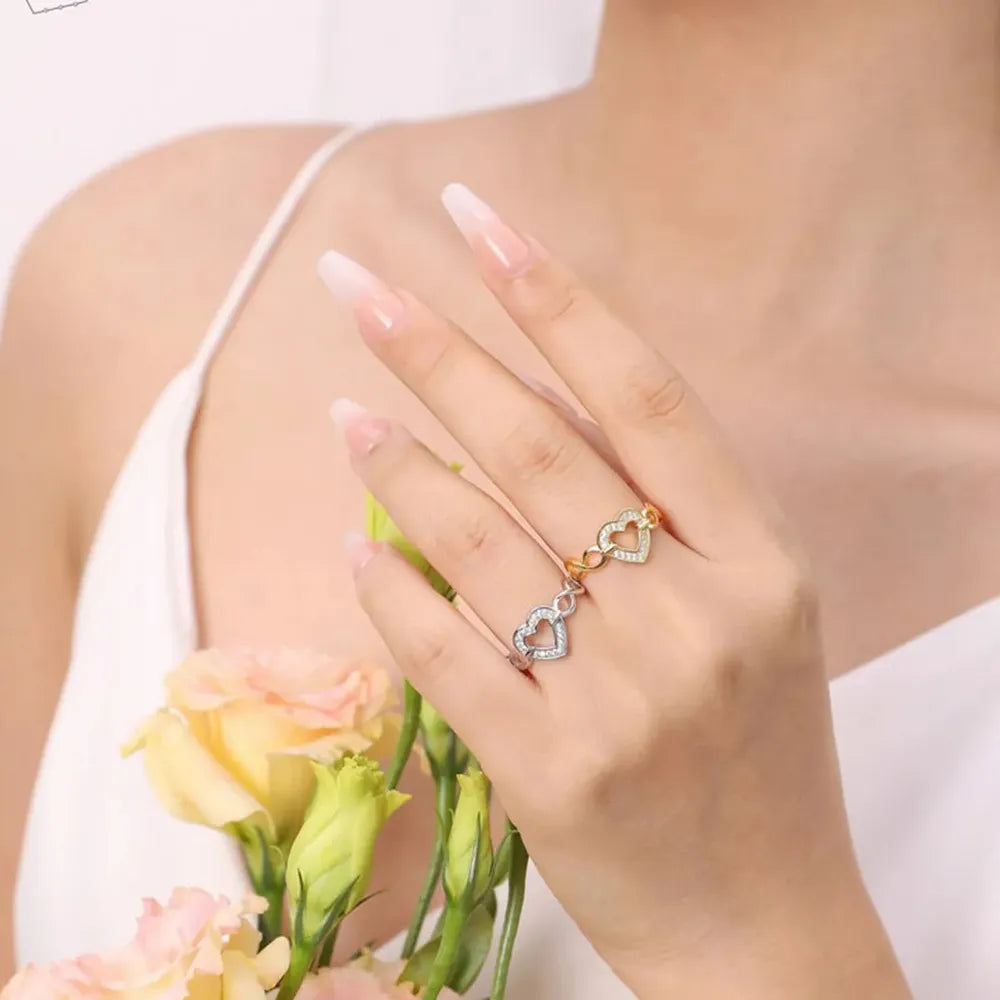 Gold and silver pavé heart rings intertwined on a woman's hand.