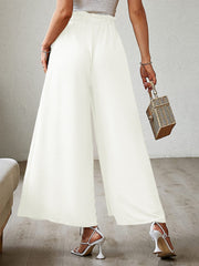 White pleated palazzo pants with a high waist and wide leg, featuring a subtle slit.