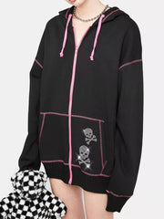 Black zip-up hoodie with pink contrast stitching, drawstring hood, and rhinestone skull graphics.