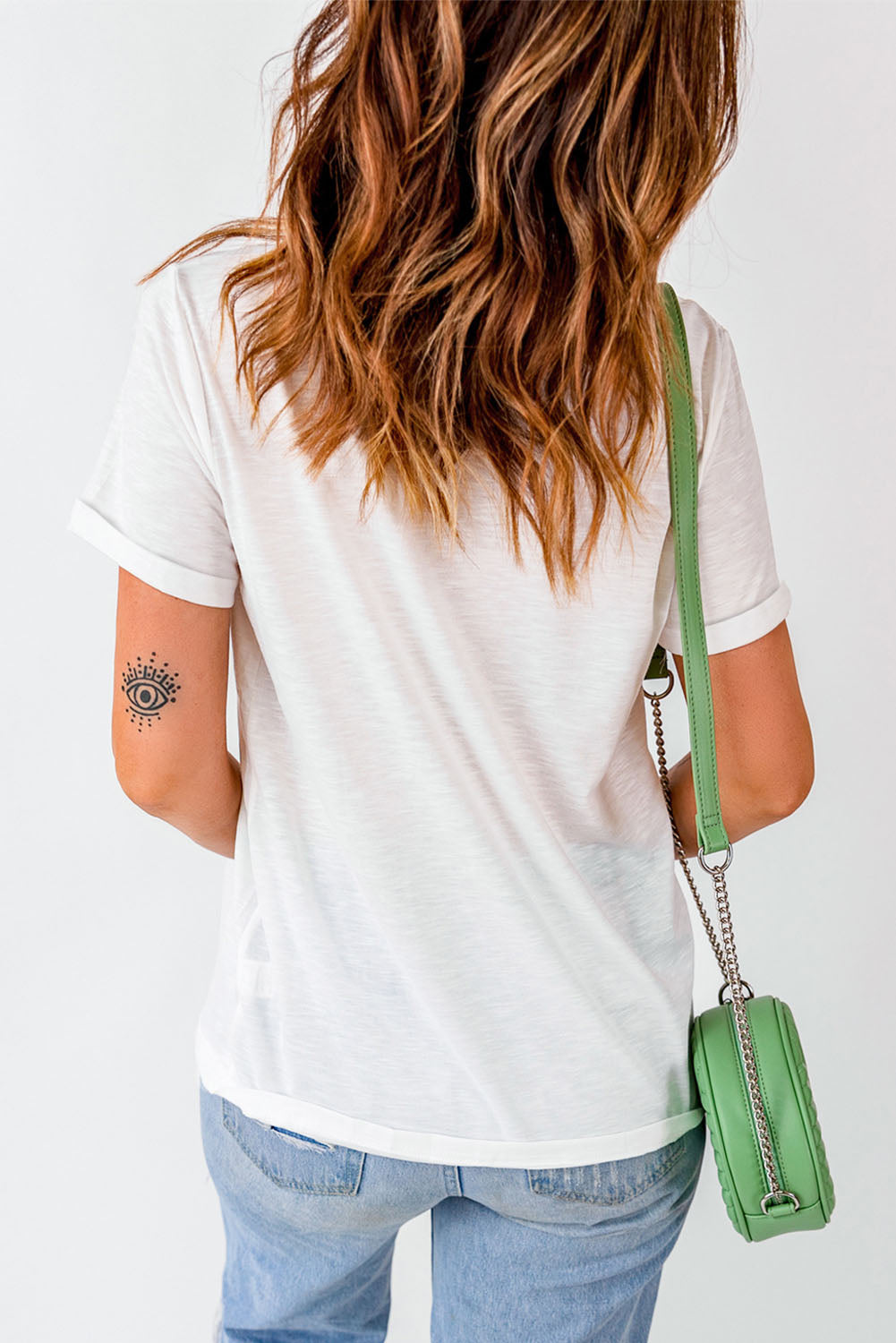 White graphic t-shirt with rolled sleeves and a casual fit, styled with jeans and a green crossbody bag.