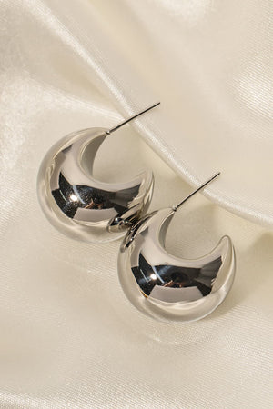 Sculptural silver crescent hoop earrings with a polished finish on satin fabric.