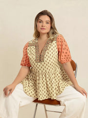 Vibrant geometric peplum shirt with coral sleeves and V-neck.