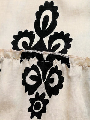 Bohemian maxi dress detail with black floral print on apricot fabric and smocked tiered skirt.
