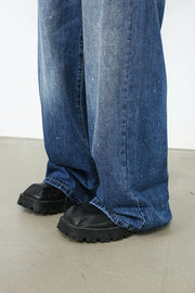 Painterly denim palazzo trousers in medium wash with white paint splatters and wide leg.