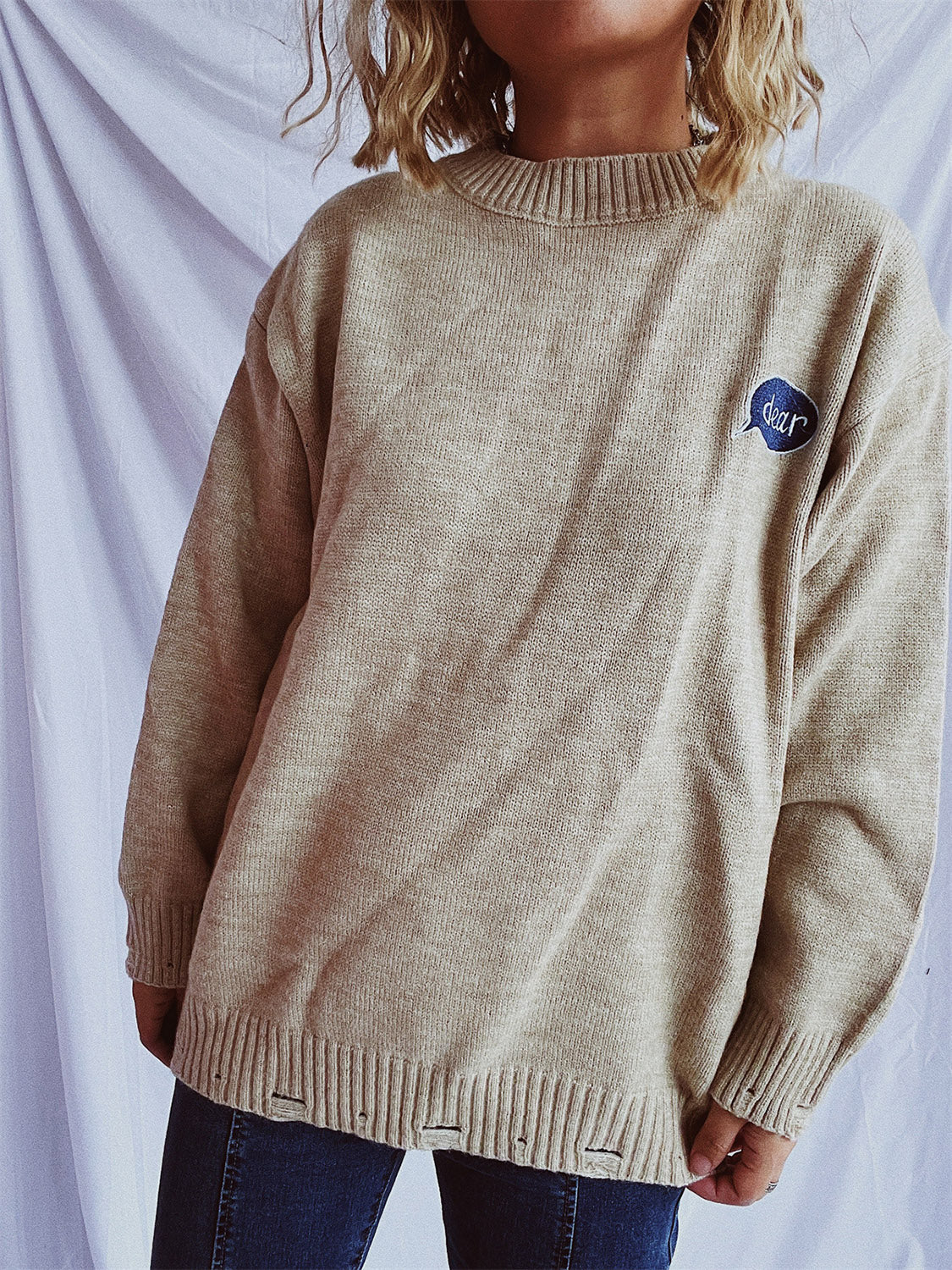 Relaxed knit sweater in dark gray or tan, acrylic, with embroidered character detail.