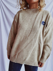 Relaxed knit sweater in dark gray or tan, acrylic, with embroidered character detail.