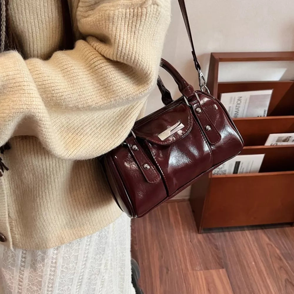 Elegant barrel crossbody bag with top handles in wine red patent leather, silver hardware.