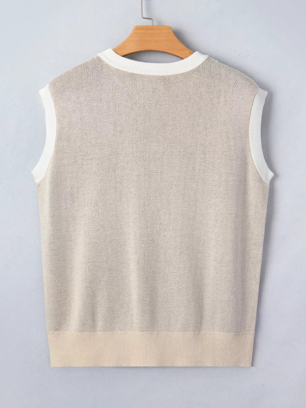 Sleeveless knit sweater vest in beige with white trim and ribbed hem.