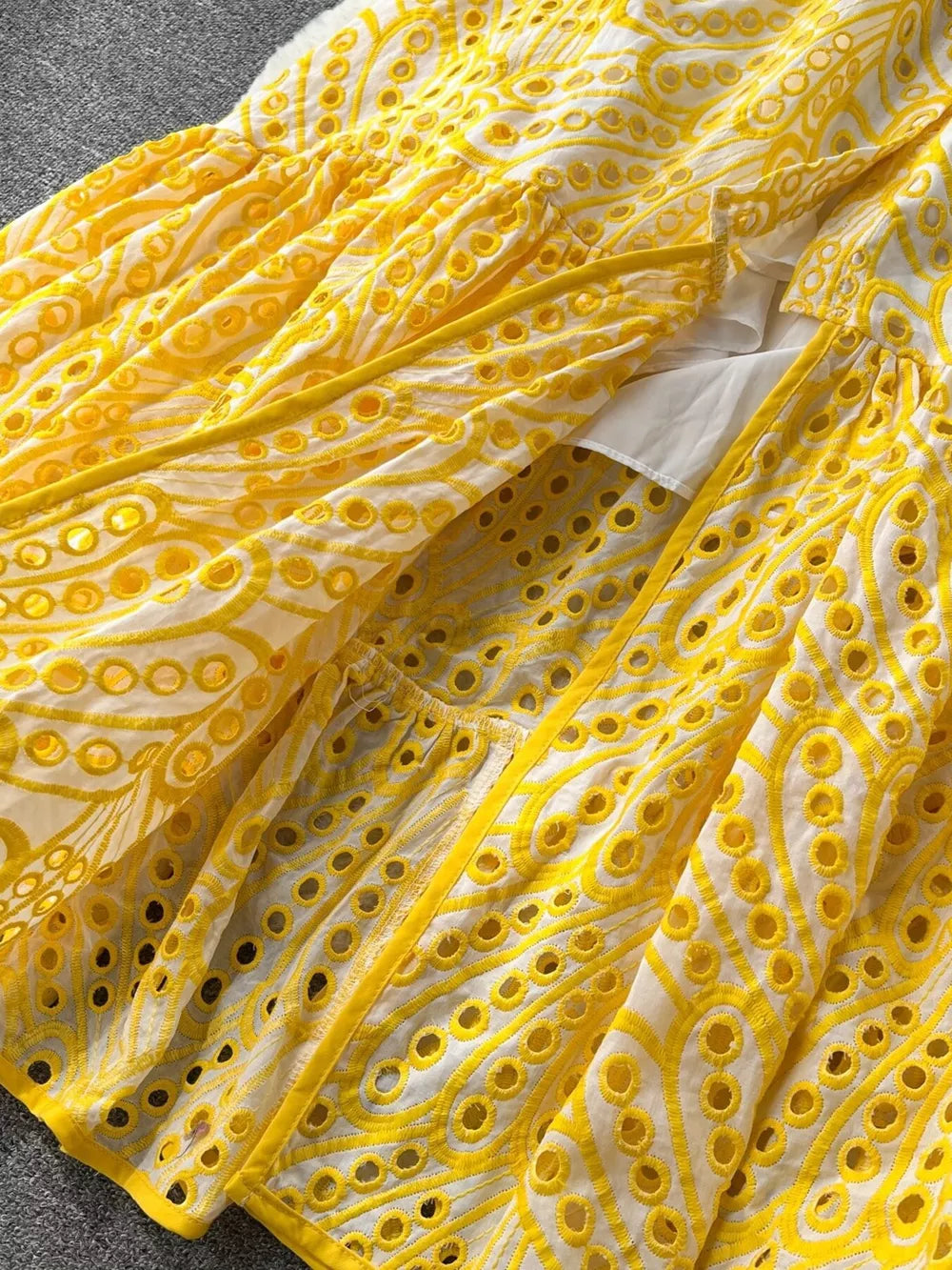 Yellow lace-embroidered tiered cami dress with eyelet details and a white underlayer.
