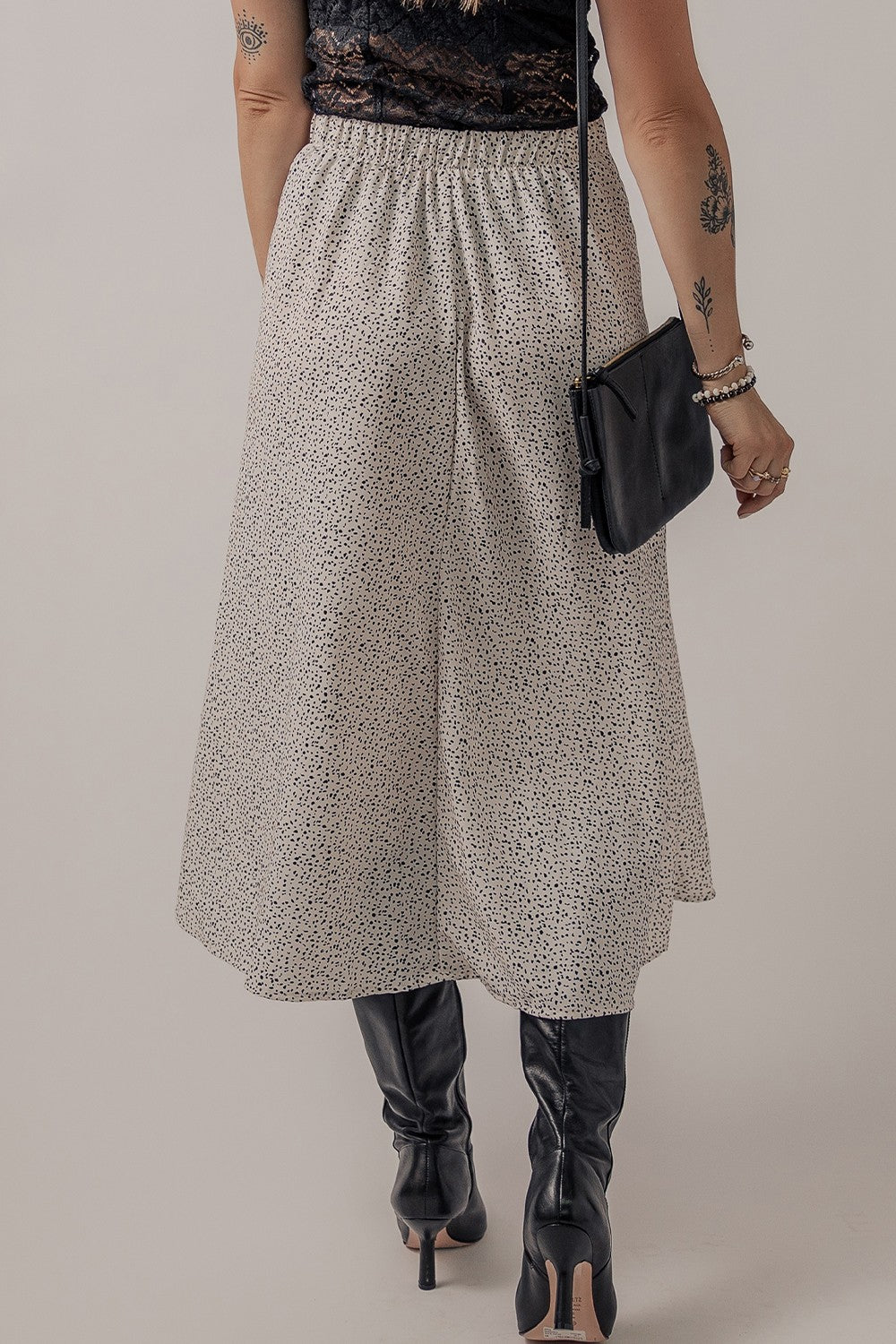 Dotted bias-cut midi skirt in heather gray with an elastic waist, styled with black boots and a crossbody bag.