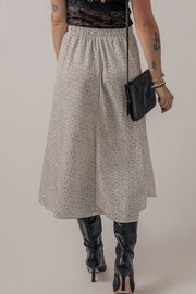 Dotted bias-cut midi skirt in heather gray with an elastic waist, styled with black boots and a crossbody bag.