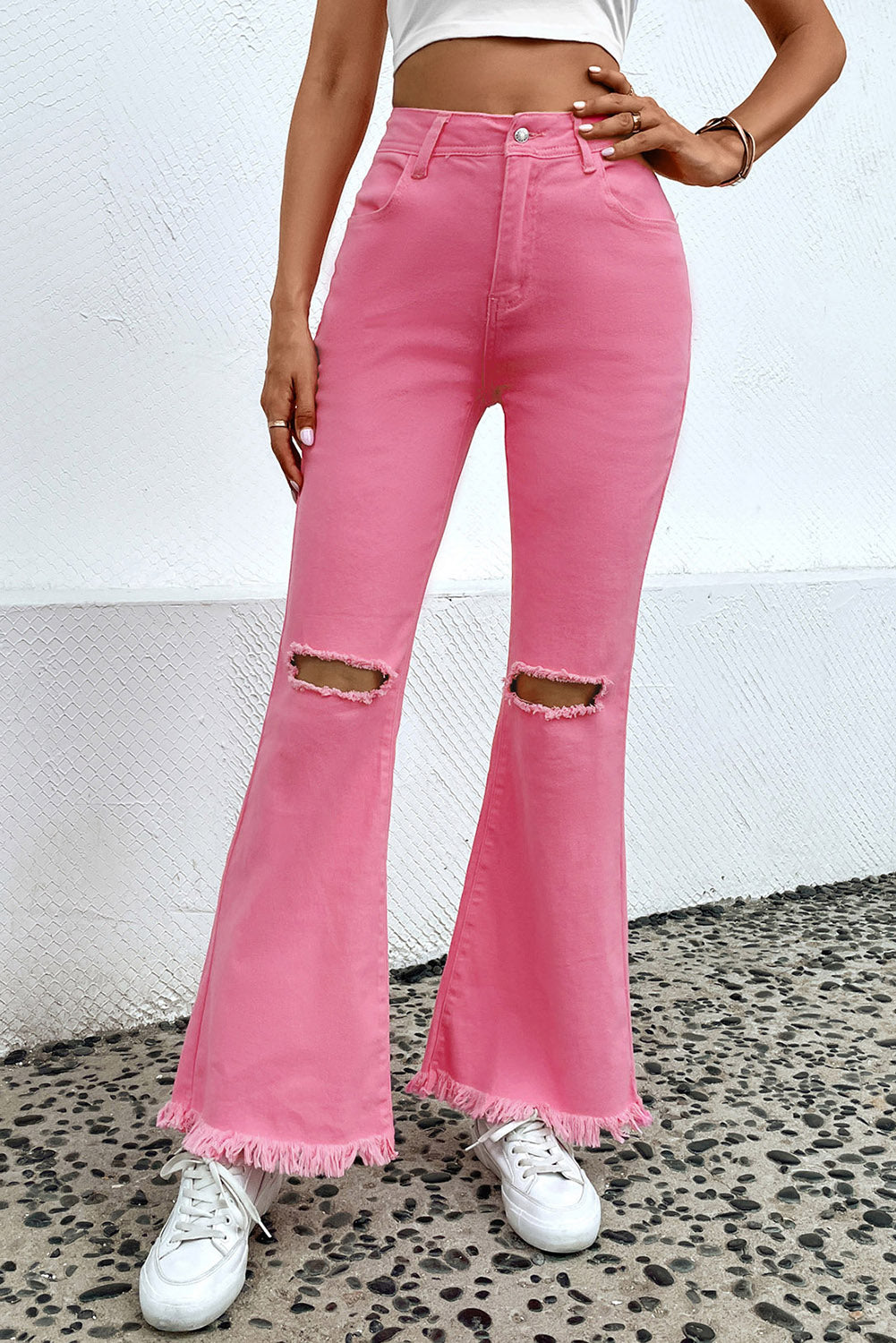 Pink flare jeans with distressed knees and raw hem, styled with white sneakers.
