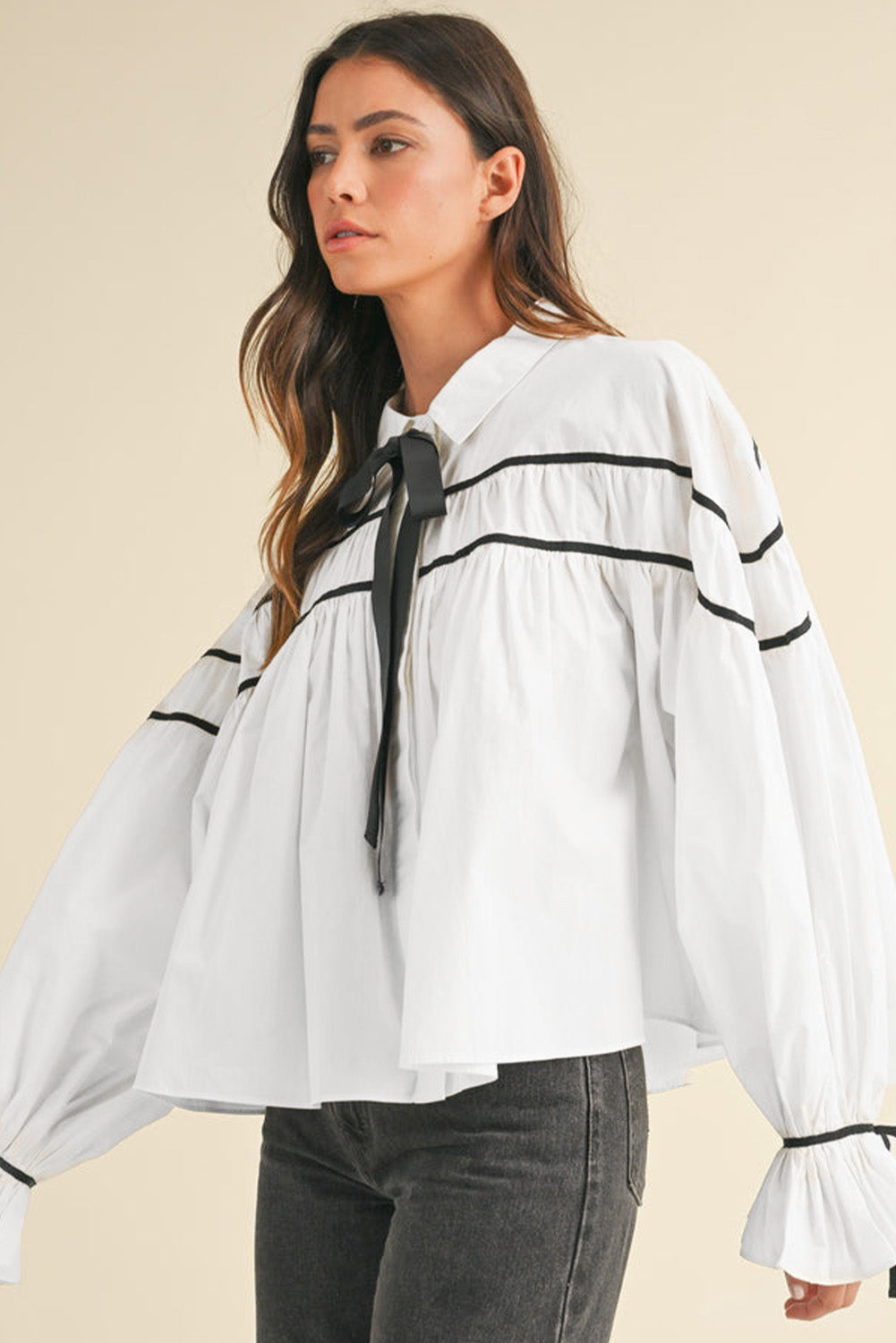 White blouse with black piped trim and bow tie detail, featuring voluminous sleeves and ruffled cuffs.