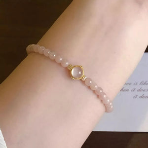 Gold-plated bracelet with blush pink beads and a central moonstone charm.