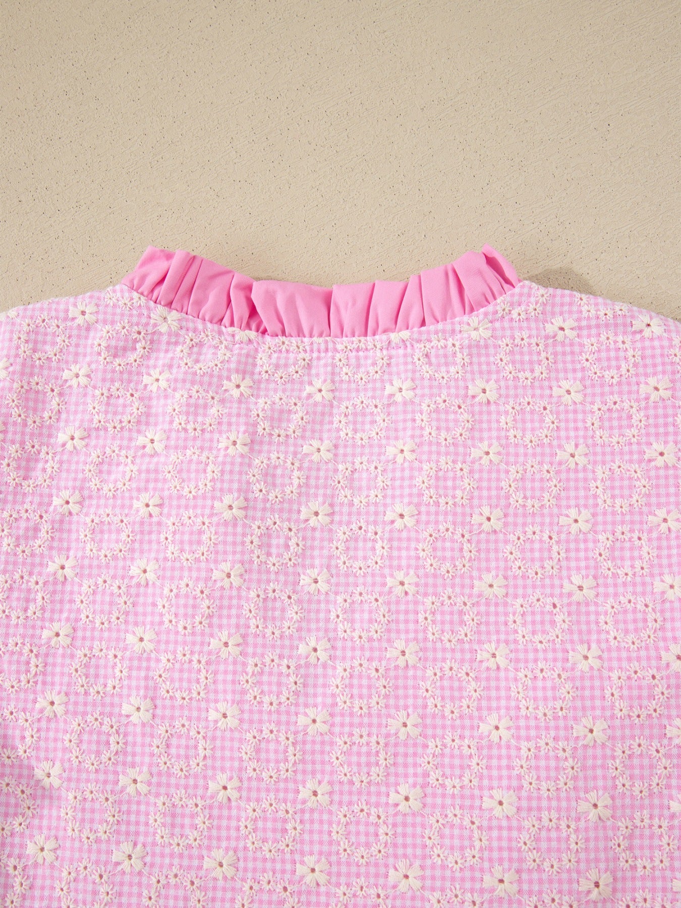 Pink gingham blouse with eyelet embroidery and ruffled neckline.