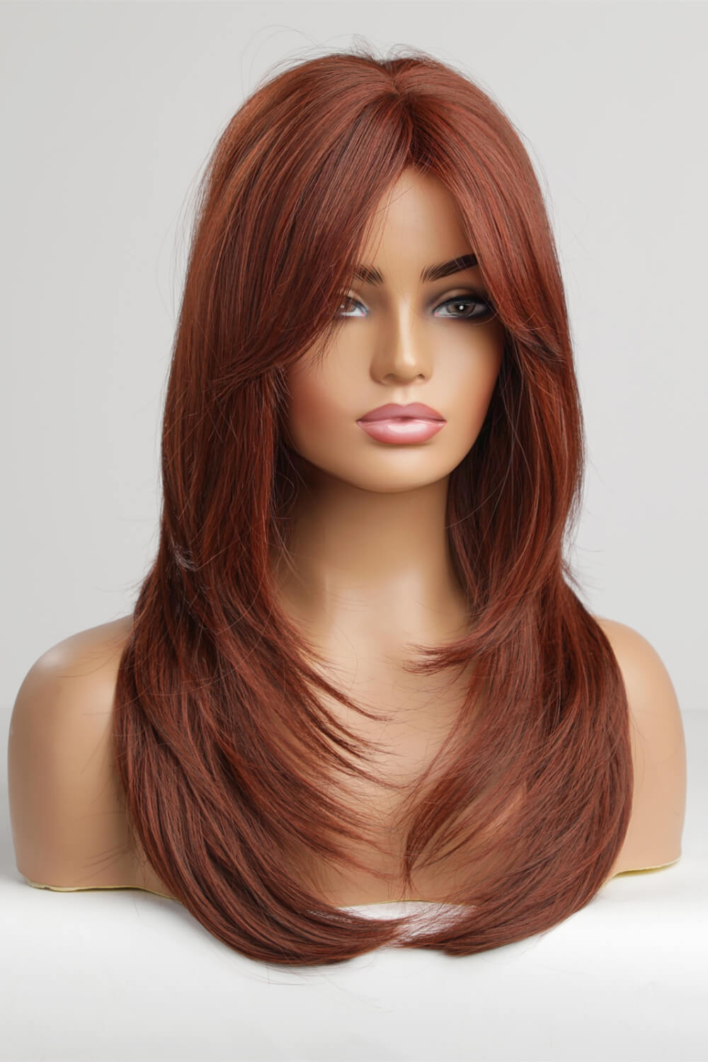 Layered copper red synthetic wig with chic bangs on a mannequin.