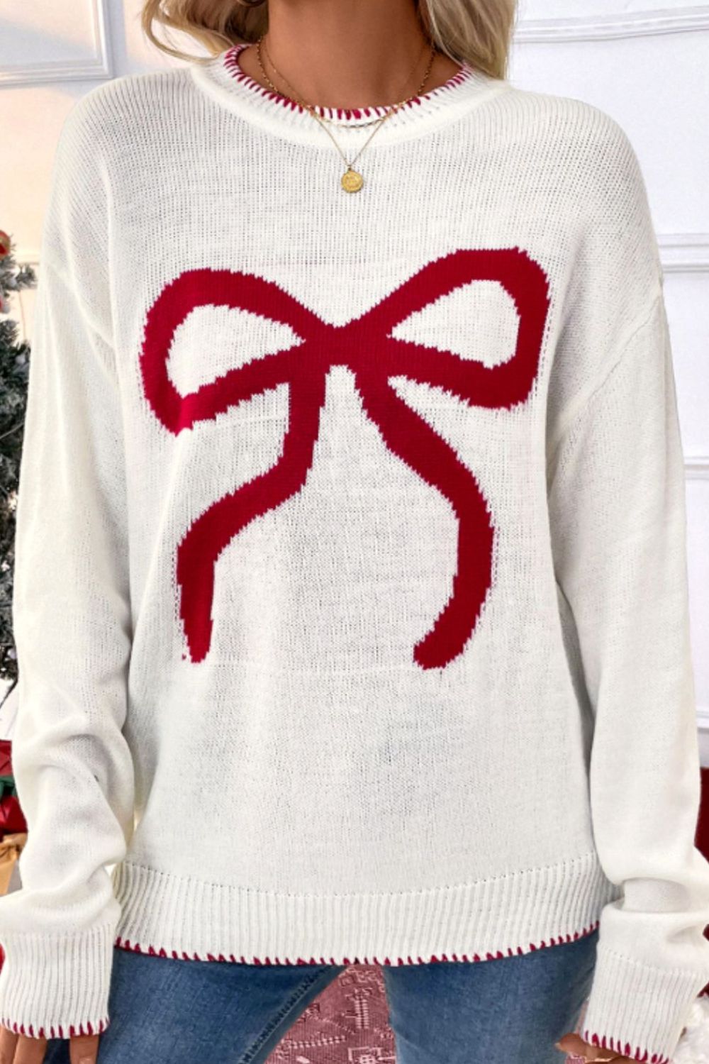 White knit sweater with a large red bow graphic and red trim.
