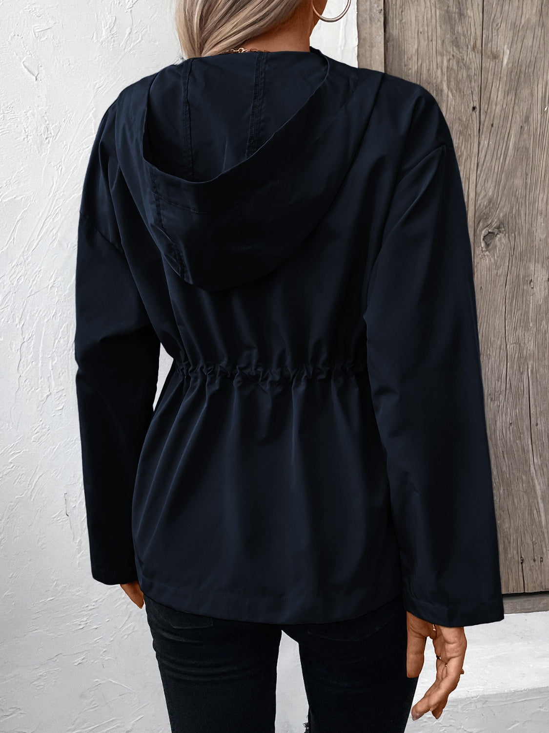 Navy utility jacket with drawstring waist and hood, shown from the back.