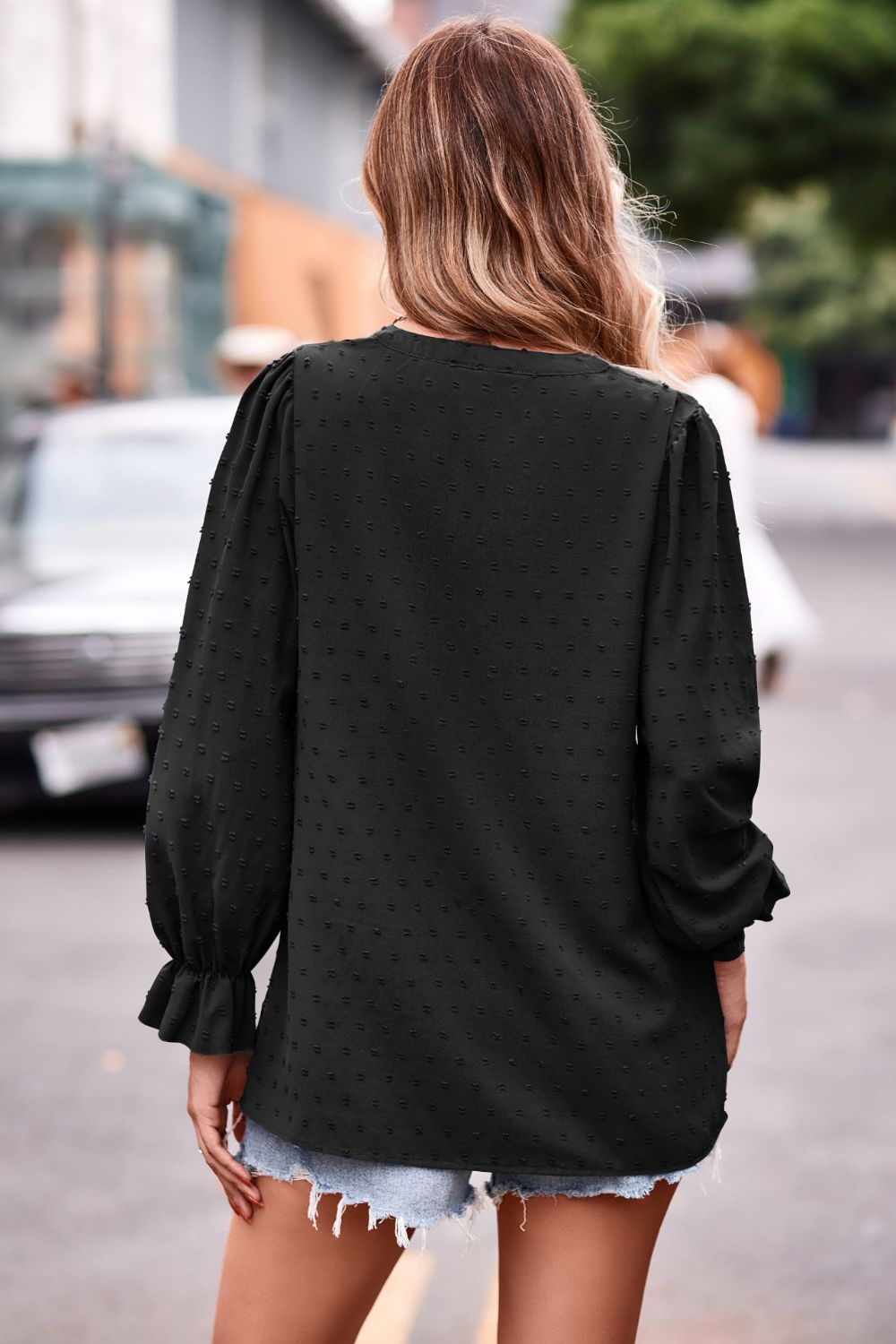 Black textured dot v-neck blouse with long puff sleeves and ruffle cuffs.