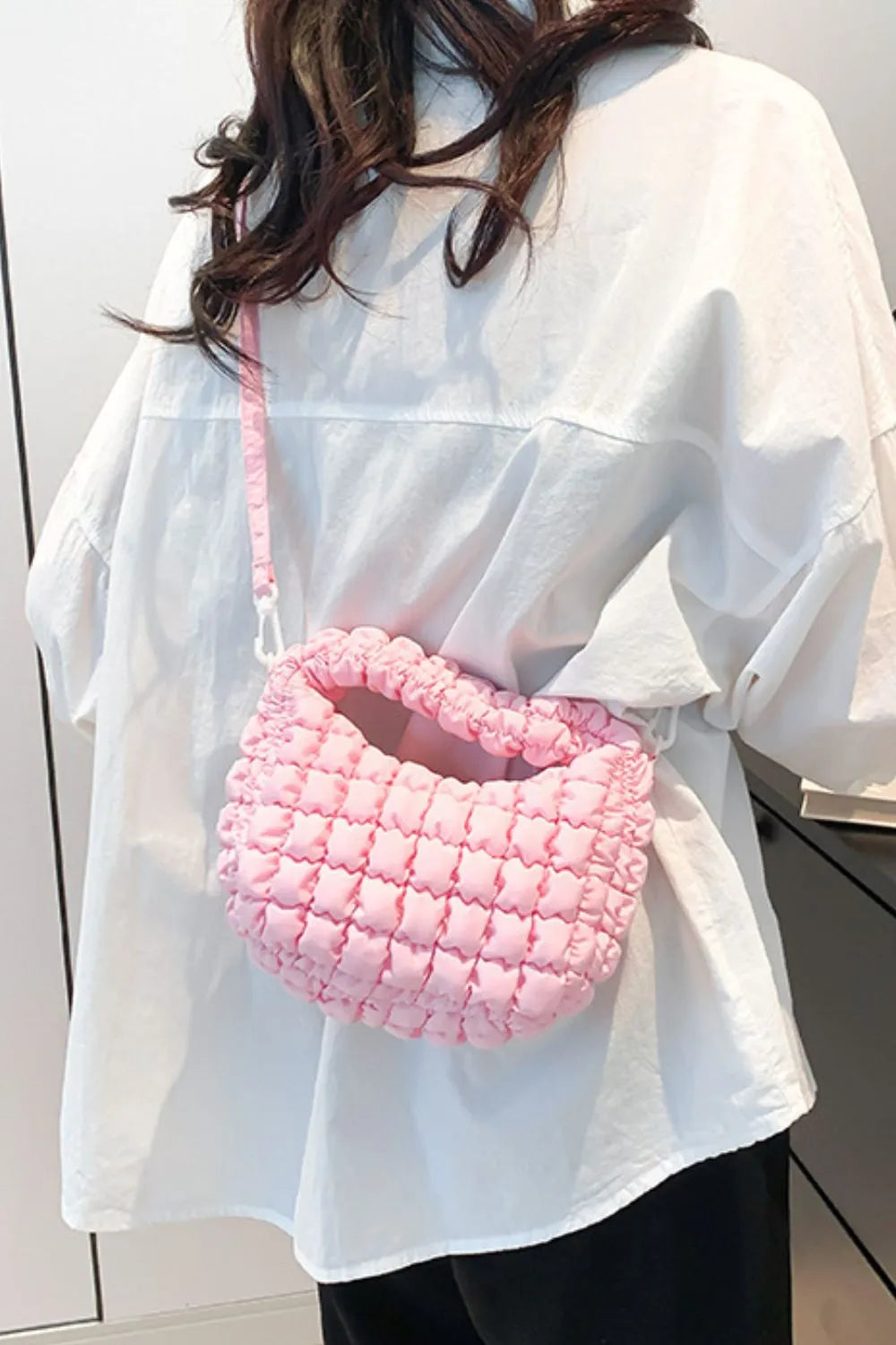 Pink padded crescent crossbody bag with sculptural texture and ruched detail.