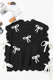 Black knit vest with white bow print, scalloped hem, and tie details on the sides.