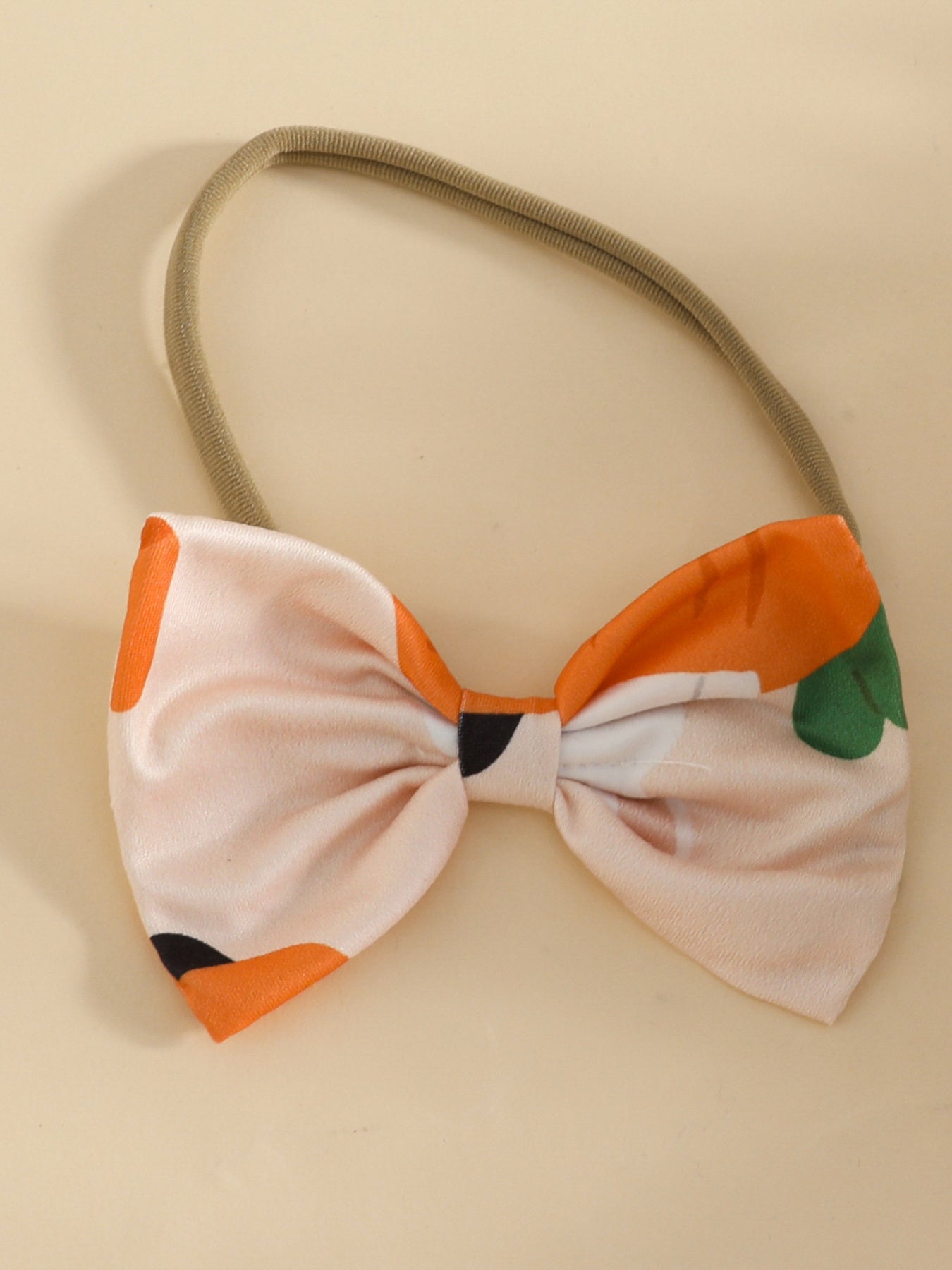 Baby bow headband with orange and pink carrot print and green leaf accents.