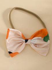 Baby bow headband with orange and pink carrot print and green leaf accents.
