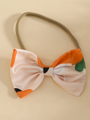 Baby bow headband with orange and pink carrot print and green leaf accents.