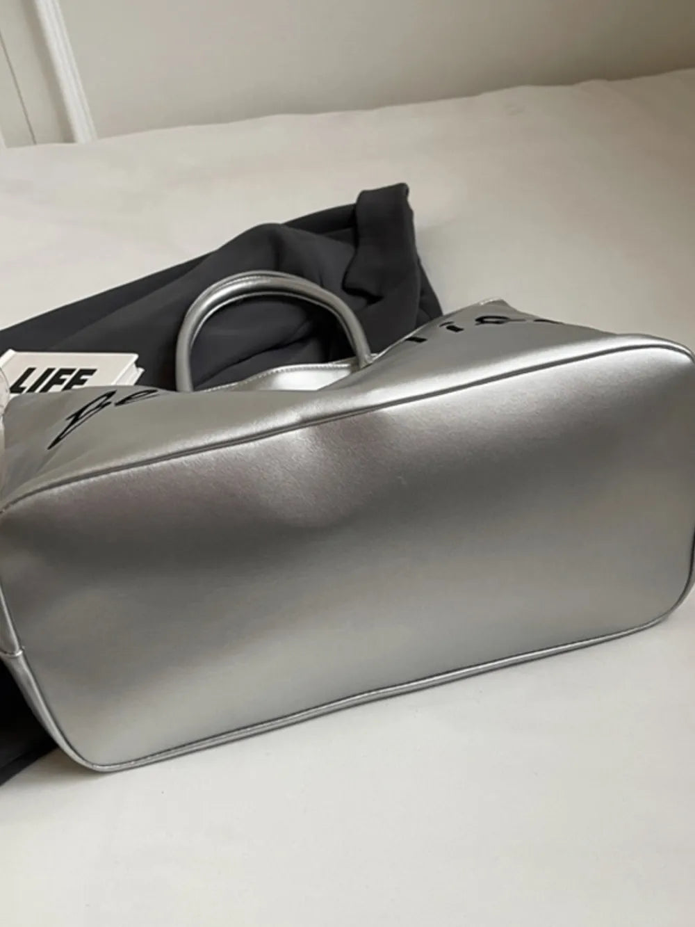 Silver metallic tote bag with black "Better Life" graphic and top handles.