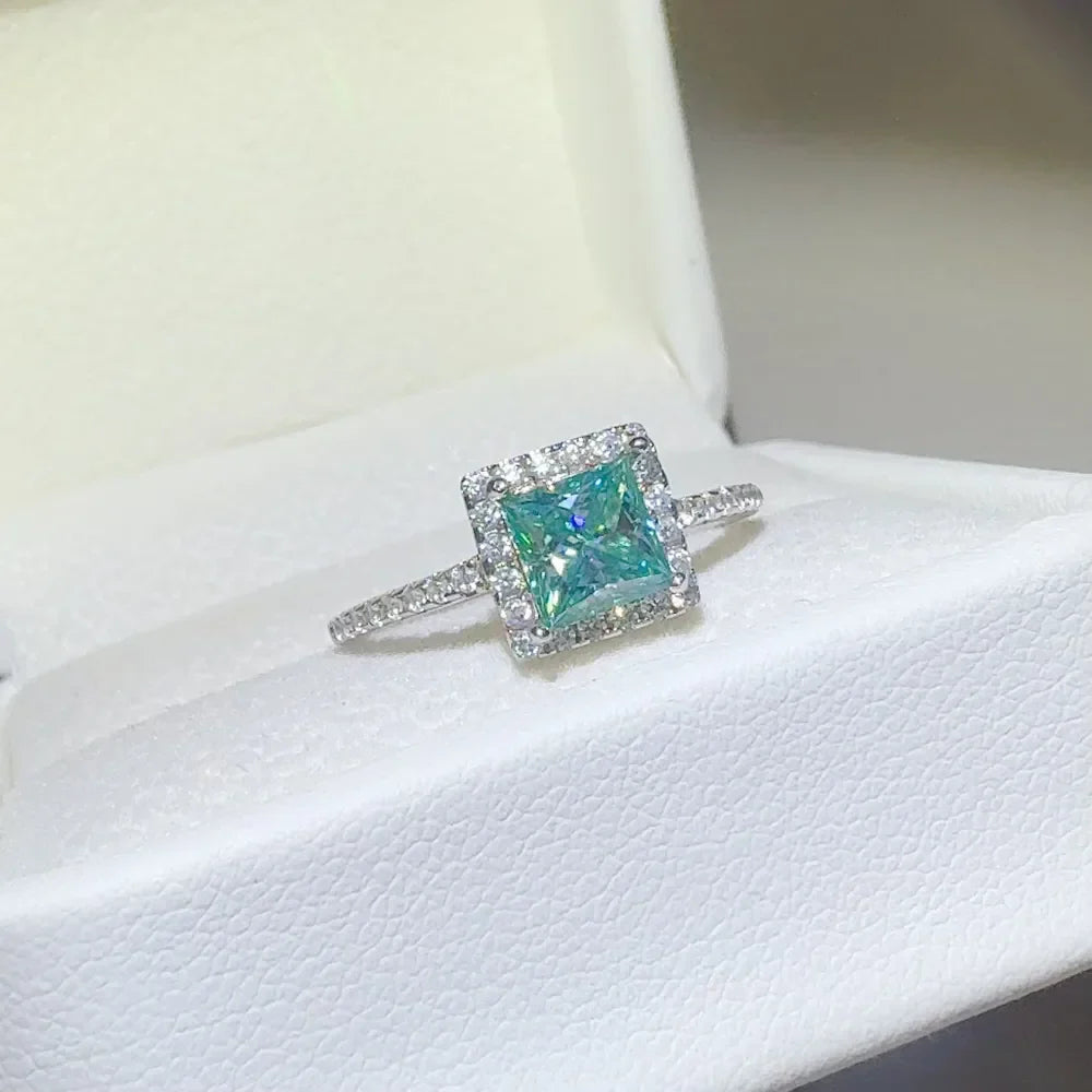 Radiant square halo moissanite ring in silver with a bright blue-green center stone.