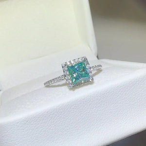 Radiant square halo moissanite ring in silver with a bright blue-green center stone.