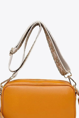 Orange textured crossbody bag with woven strap detail and tassel.