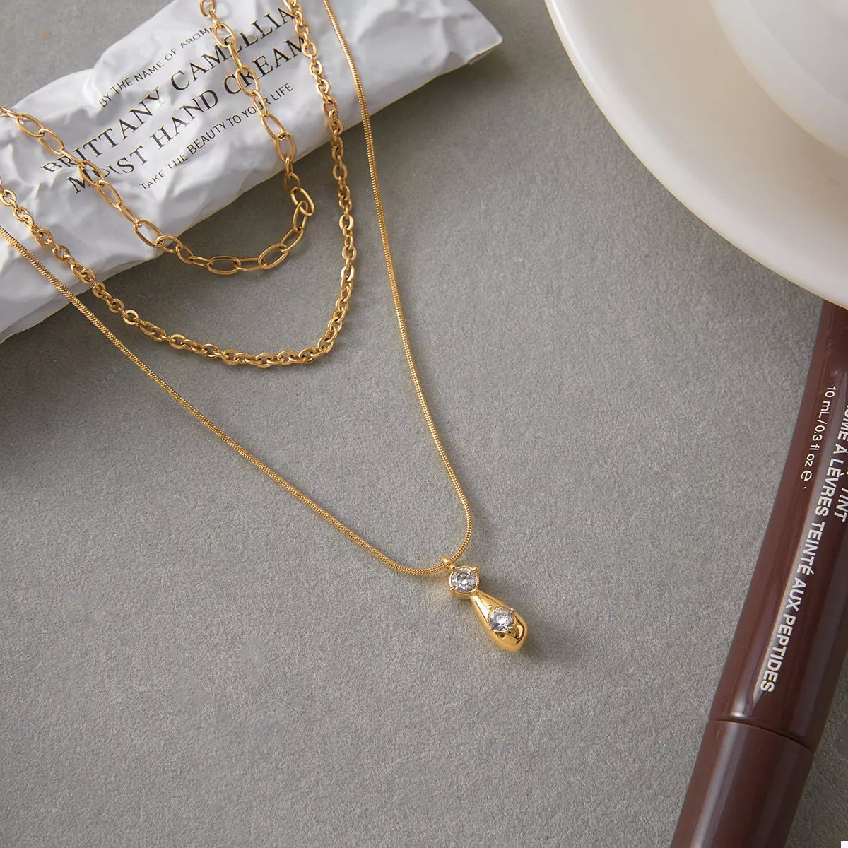Gold three-layered pendant necklace with two clear stones and a teardrop pendant.