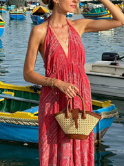 Red paisley print backless maxi dress with halter neckline, styled with a straw tote bag.