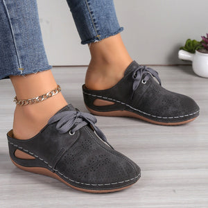 Dark gray perforated slip-on mules with lace-up detail and white stitching.