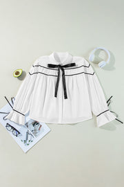 White blouse with black piped trim and bow detail, long sleeves with ruffled cuffs.
