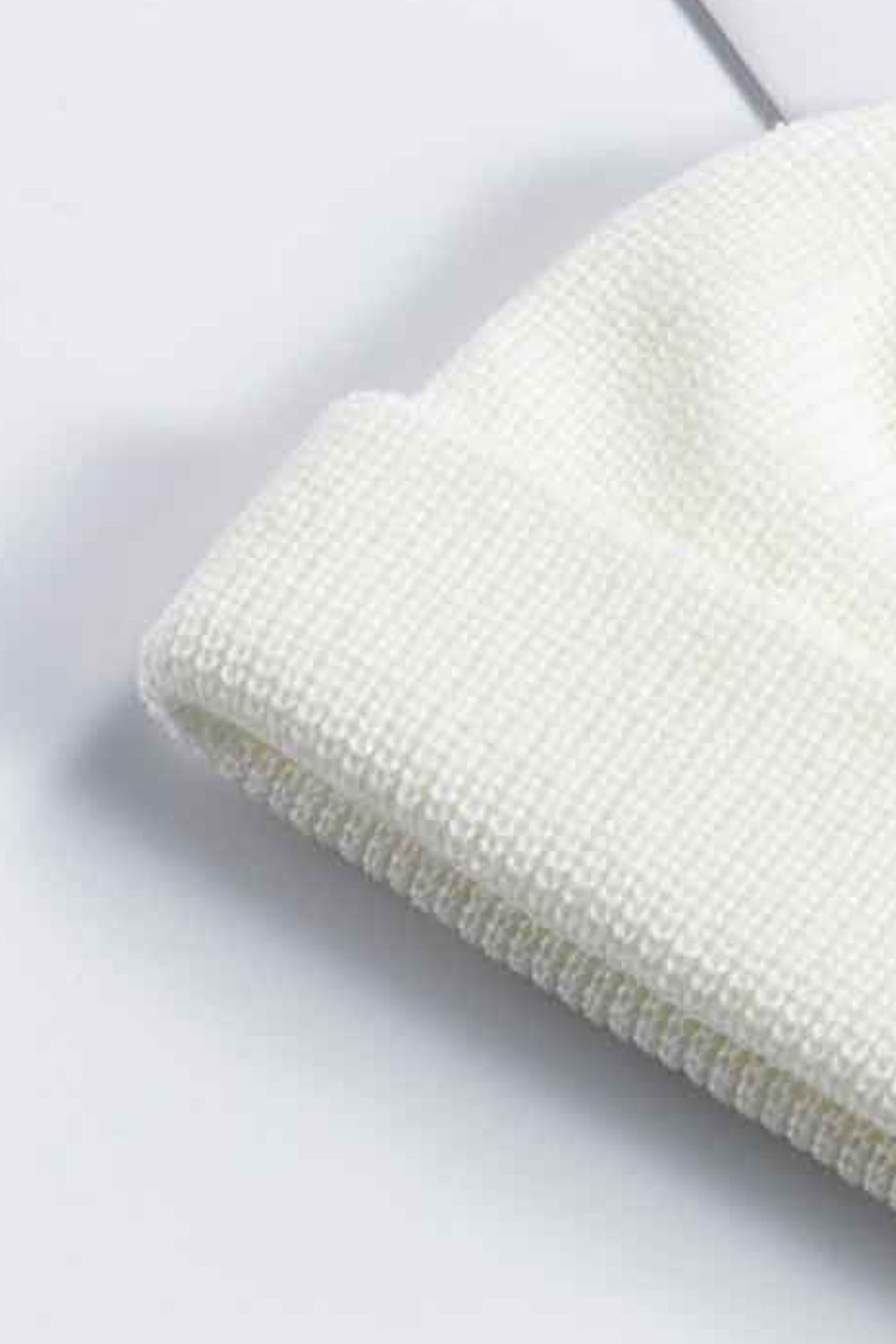 White ribbed knit beanie with a turn-up cuff, acrylic material.