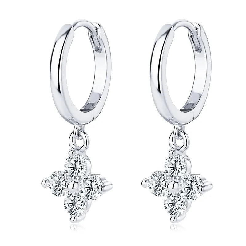 Silver huggie hoop earrings with dangling clover charms set with clear stones.