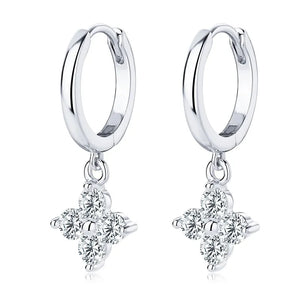 Silver huggie hoop earrings with dangling clover charms set with clear stones.