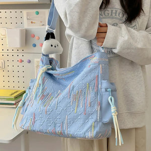 Light blue slouchy shoulder bag with quilted pattern and colorful embroidered details.