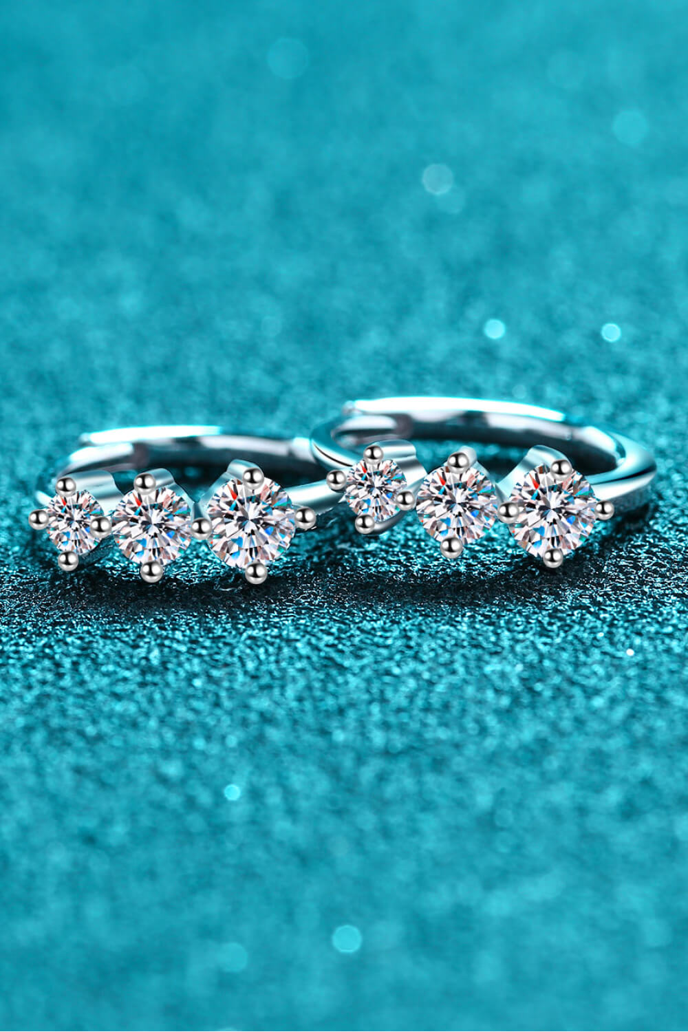 Silver huggie earrings with a triple stone cluster design, featuring sparkling clear gems.