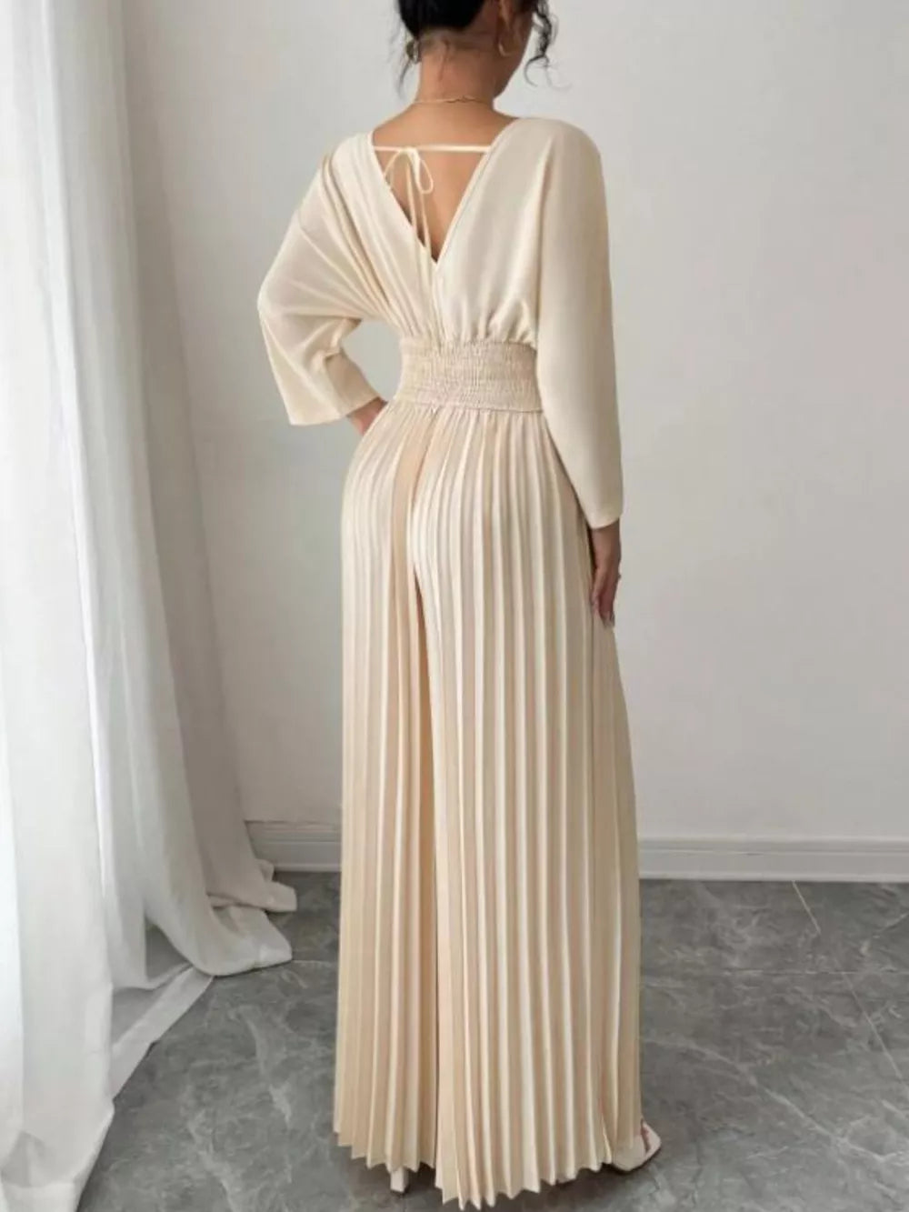 Beige pleated wide-leg jumpsuit with cinched waist and V-neck back tie detail