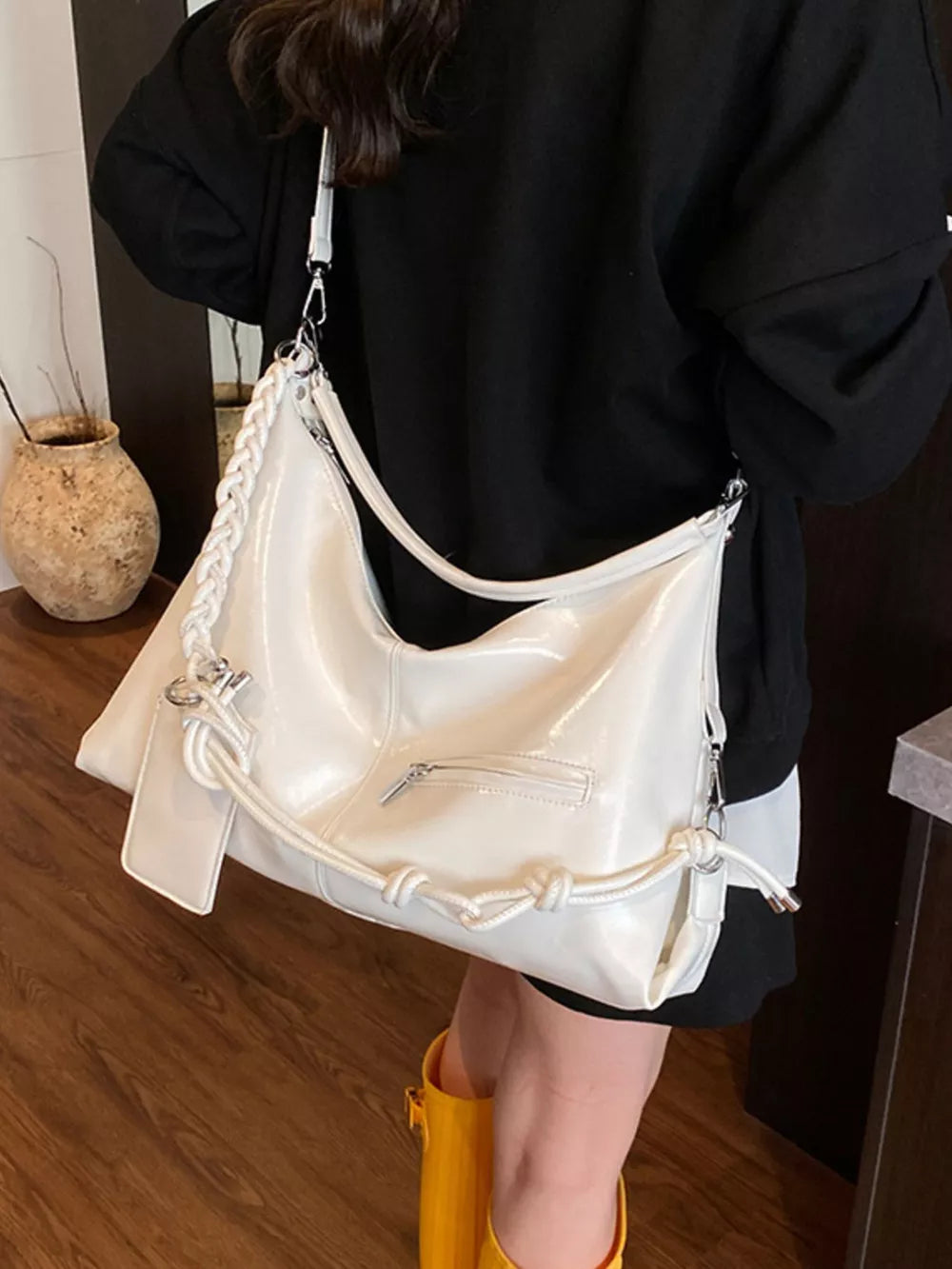 White shoulder bag with braided strap and knot details, featuring a zippered pocket.