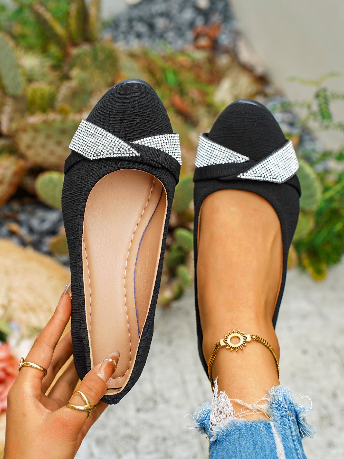 Black slip-on flats with rhinestone bow detail and textured fabric.