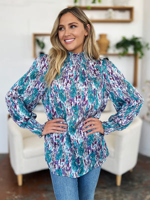 High neck abstract print blouse with smocked collar and cuffs in blue and violet tones.