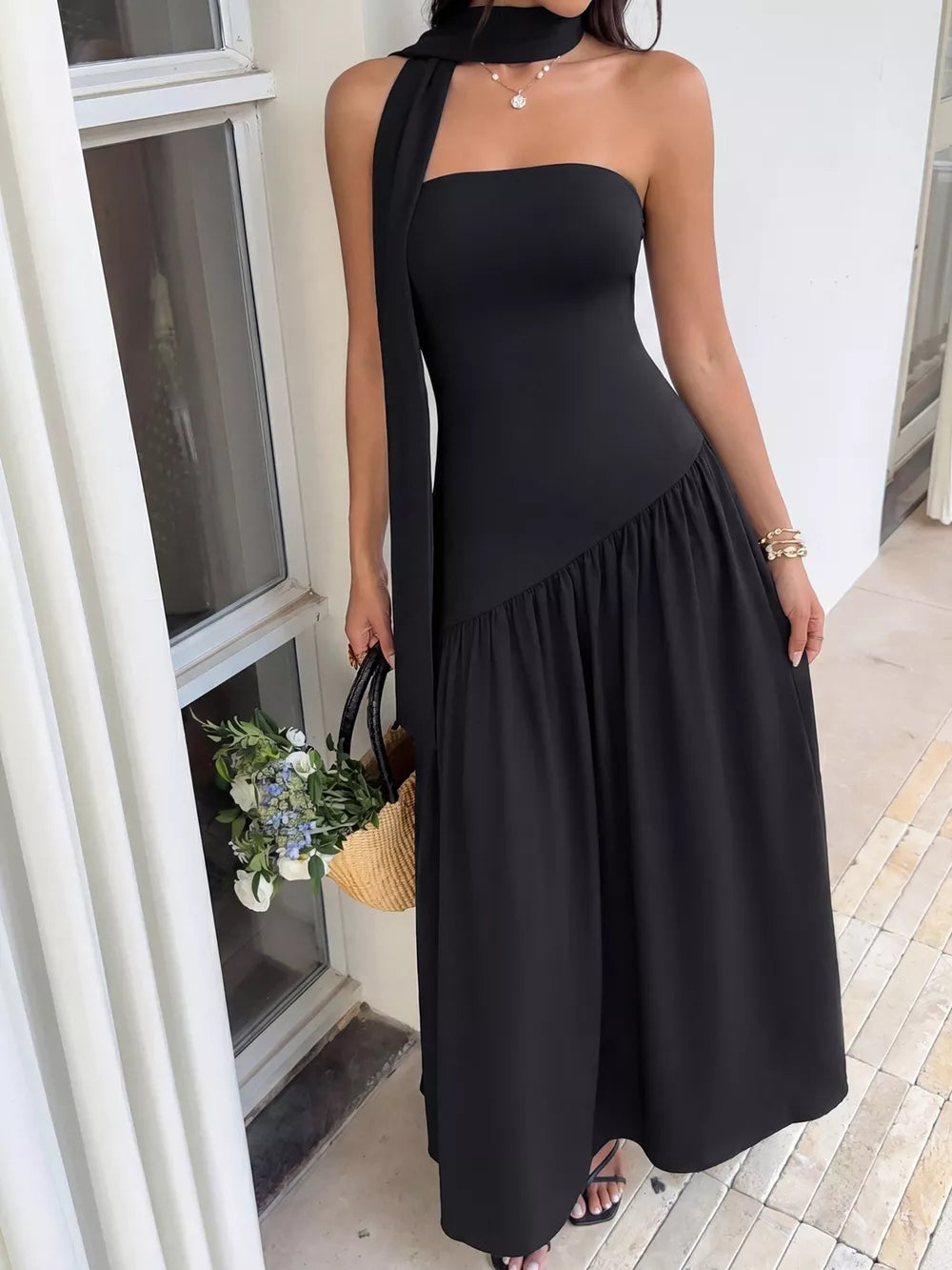 Black strapless maxi dress with asymmetrical ruffled hem and matching scarf detail.