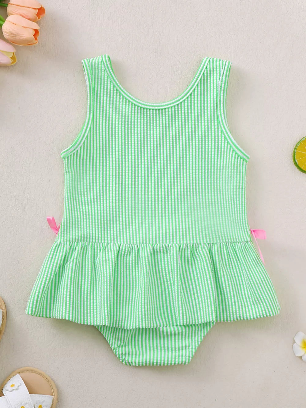 Green striped seersucker one-piece swimsuit with ruffled hem and pink side bows.