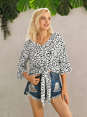 Spotted knot-front blouse with flared sleeves and V-neck, tied at waist.