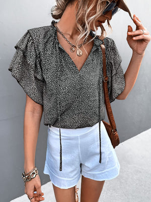 Black ditsy print blouse with ruffle sleeves and V-neck, styled with white shorts.